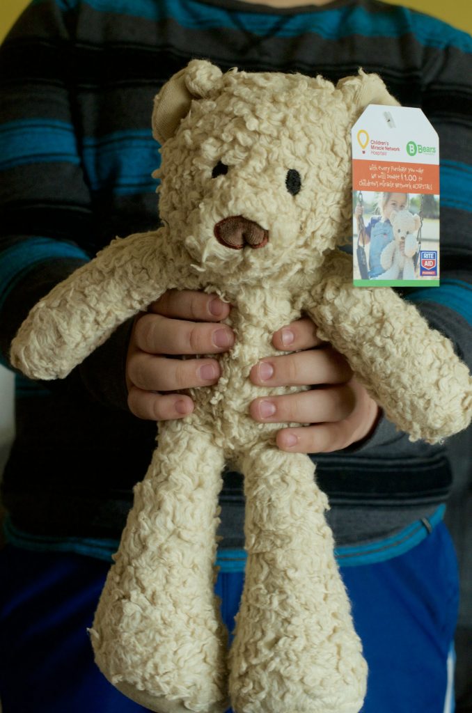 child's hands holding cream brown teddy bear plush