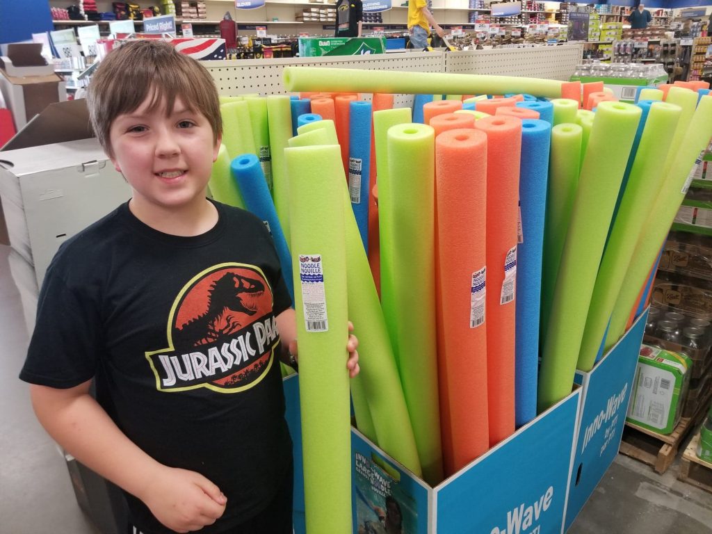 boy standing next to pool noodles at Theisen's