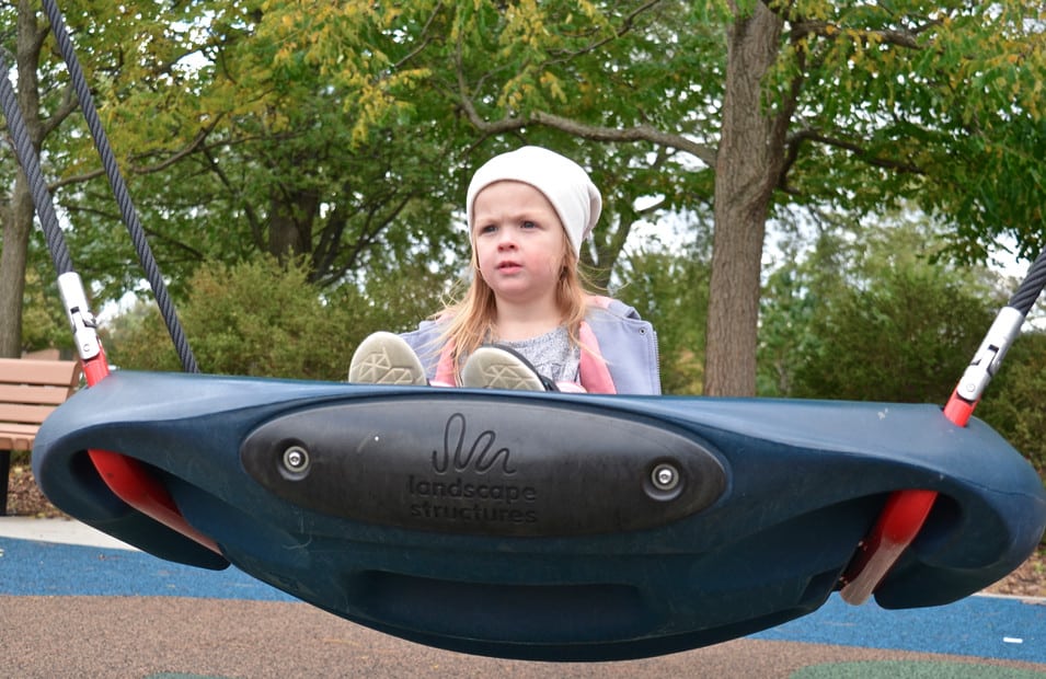 little girl in white hat on disc swing