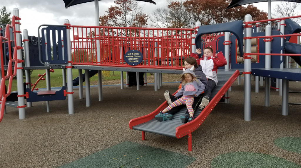 siblings children on roller slide at inclusive playground