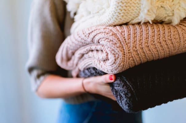 women holding pile of knitted winter sweaters