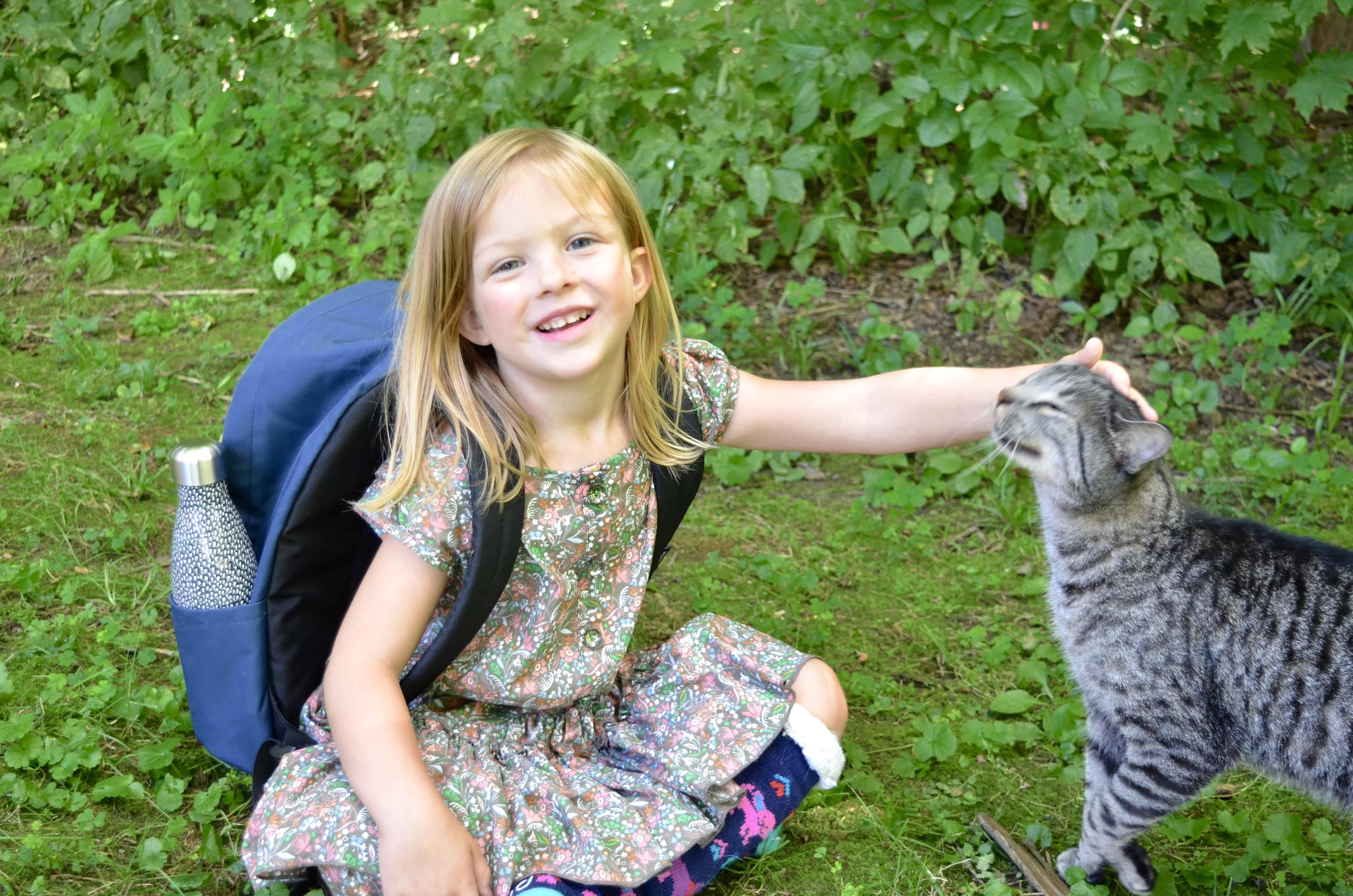 preschool girl wearing backpack petting cat