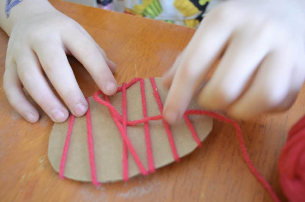 child wrapping yarn around cardboard